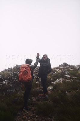 Buy stock photo Shot of two male friends giving each other a high-five while out hiking in the mountains