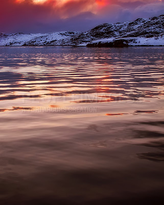 Buy stock photo Peaceful ocean landscape in winter with snowy mountains on a calm empty sea at sunset. Stunning red and yellow light reflecting on the water from the midnight sun in an arctic scene with copy space.
