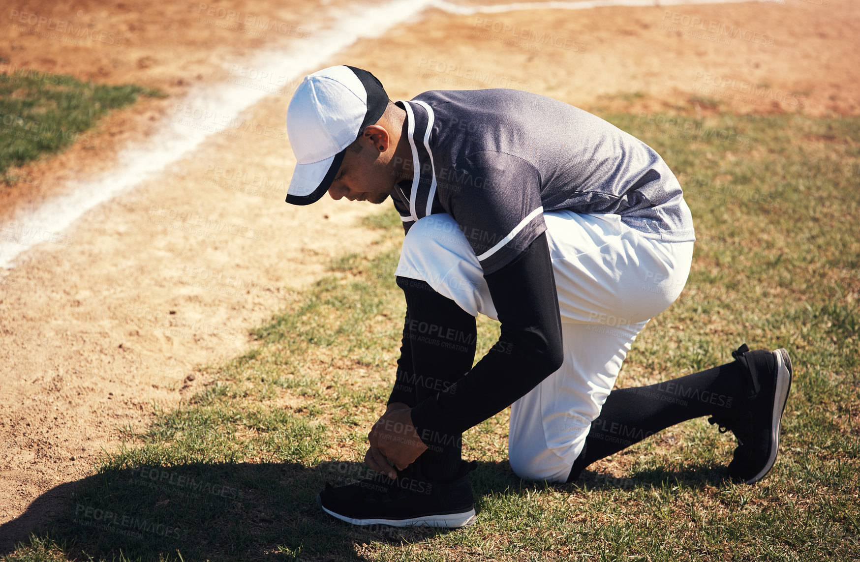 Buy stock photo Shot of a young man tying his shoelaces before playing a game of baseball