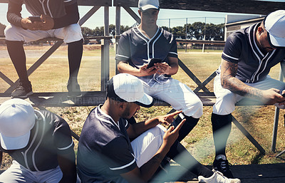 Buy stock photo Shot of a young man using a smartphone at a baseball game surrounded by his team mates