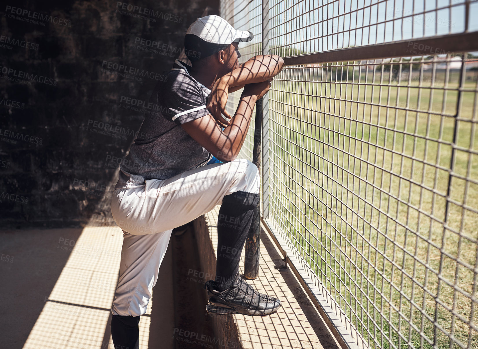 Buy stock photo Shot of a young man watching a game of baseball from behind the fence
