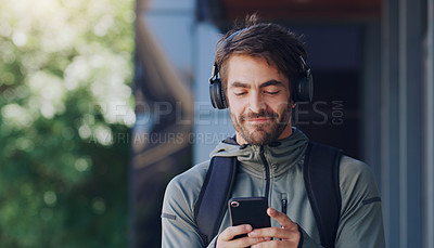 Buy stock photo Shot of a man walking outside wearing headphones and using his cellphone