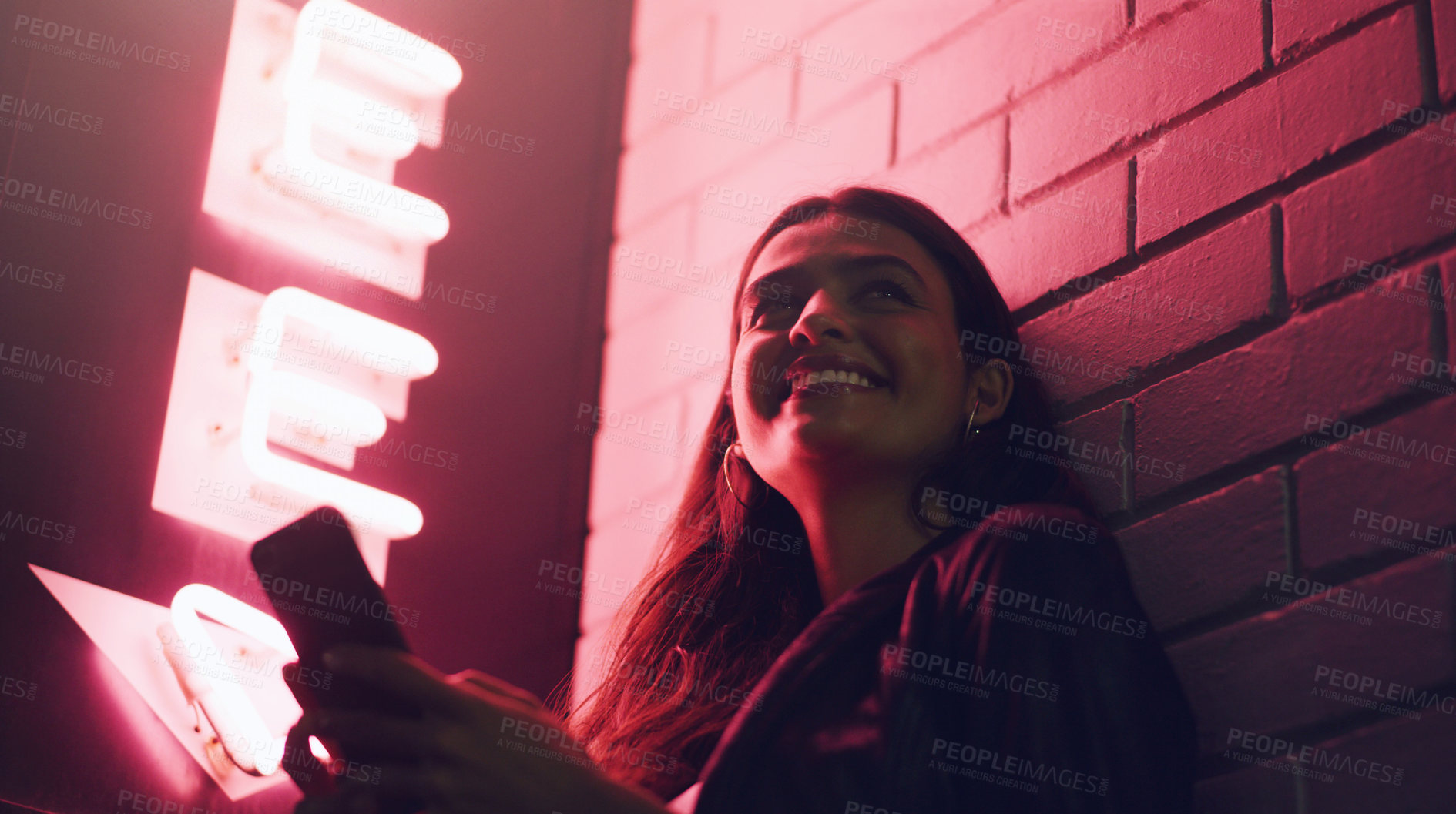 Buy stock photo Shot of a young woman using her cellphone while standing outside a building at night
