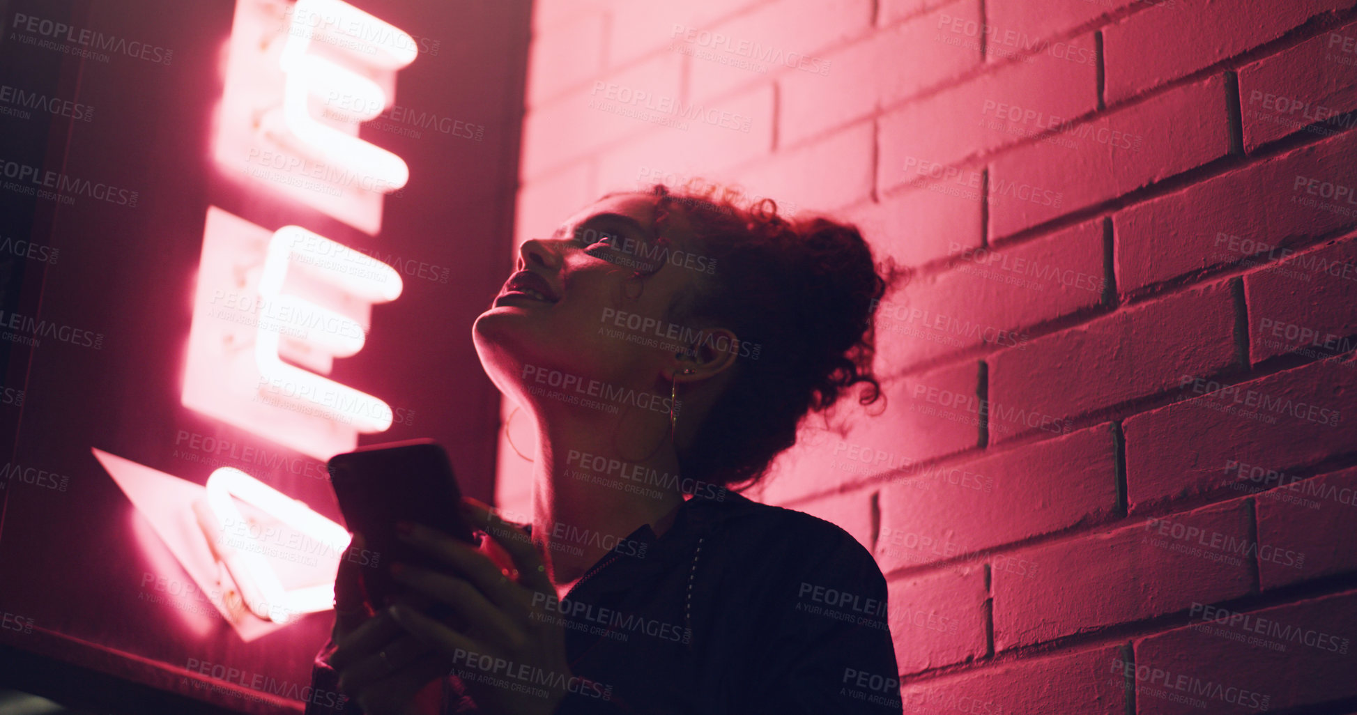 Buy stock photo Shot of a young woman using her cellphone while standing outside a building at night