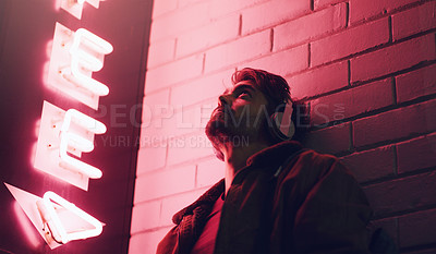 Buy stock photo Shot of a young man wearing headphones while leaning against a building at nighttime