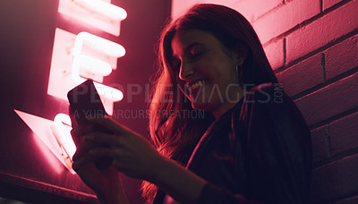 Buy stock photo Shot of a young woman using her cellphone while standing  outside a building at night