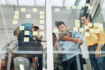 Buy stock photo Shot of a group of businesspeople using a digital tablet while brainstorming with notes on a glass wall in an office