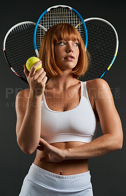 Buy stock photo Cropped shot of a woman posing with a tennis racket and ball against a dark background
