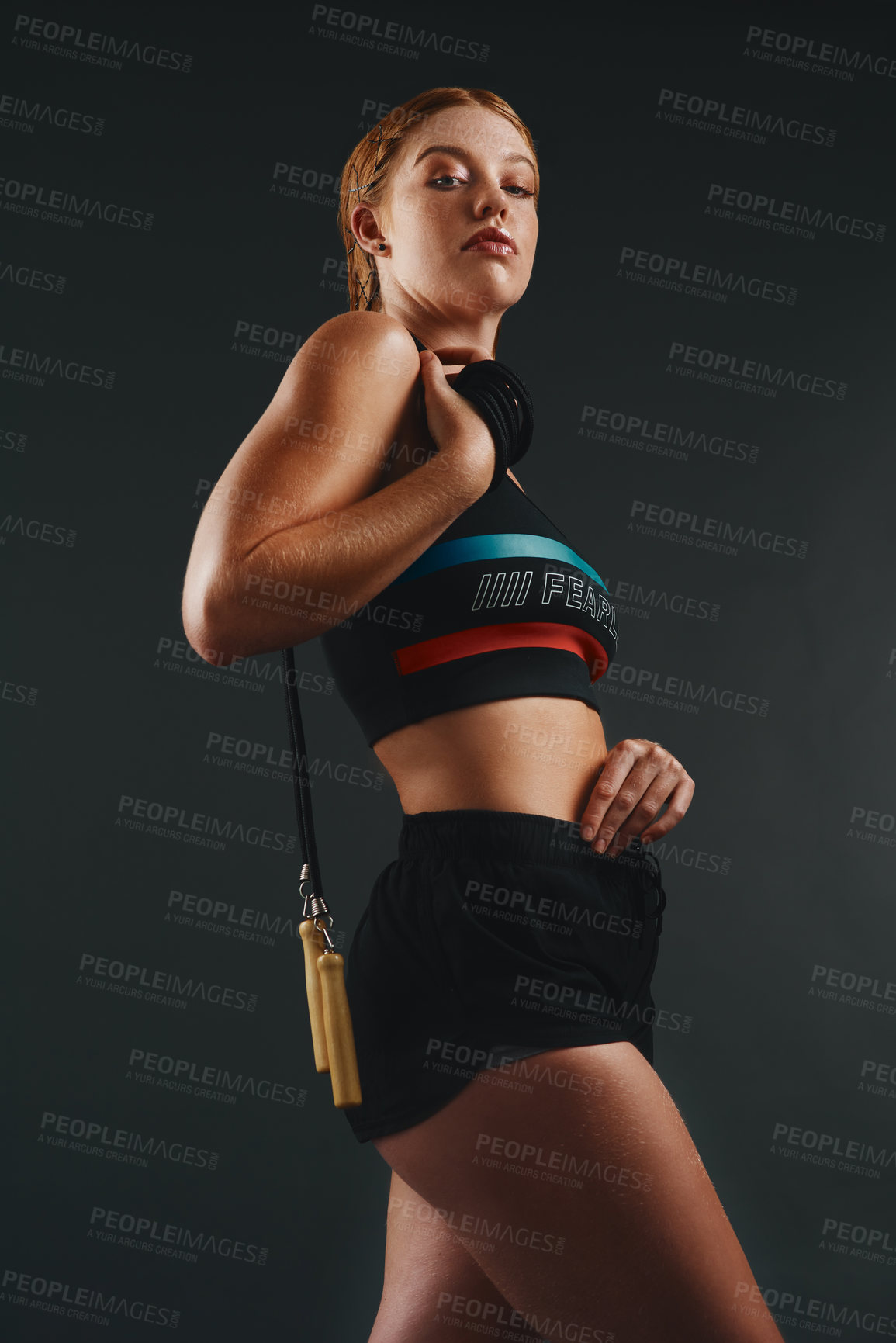 Buy stock photo Studio portrait of a sporty young woman posing with a skipping rope against a black background