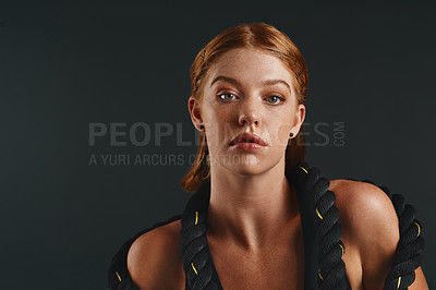 Buy stock photo Studio portrait of a sporty young woman posing with a battle rope against a black background