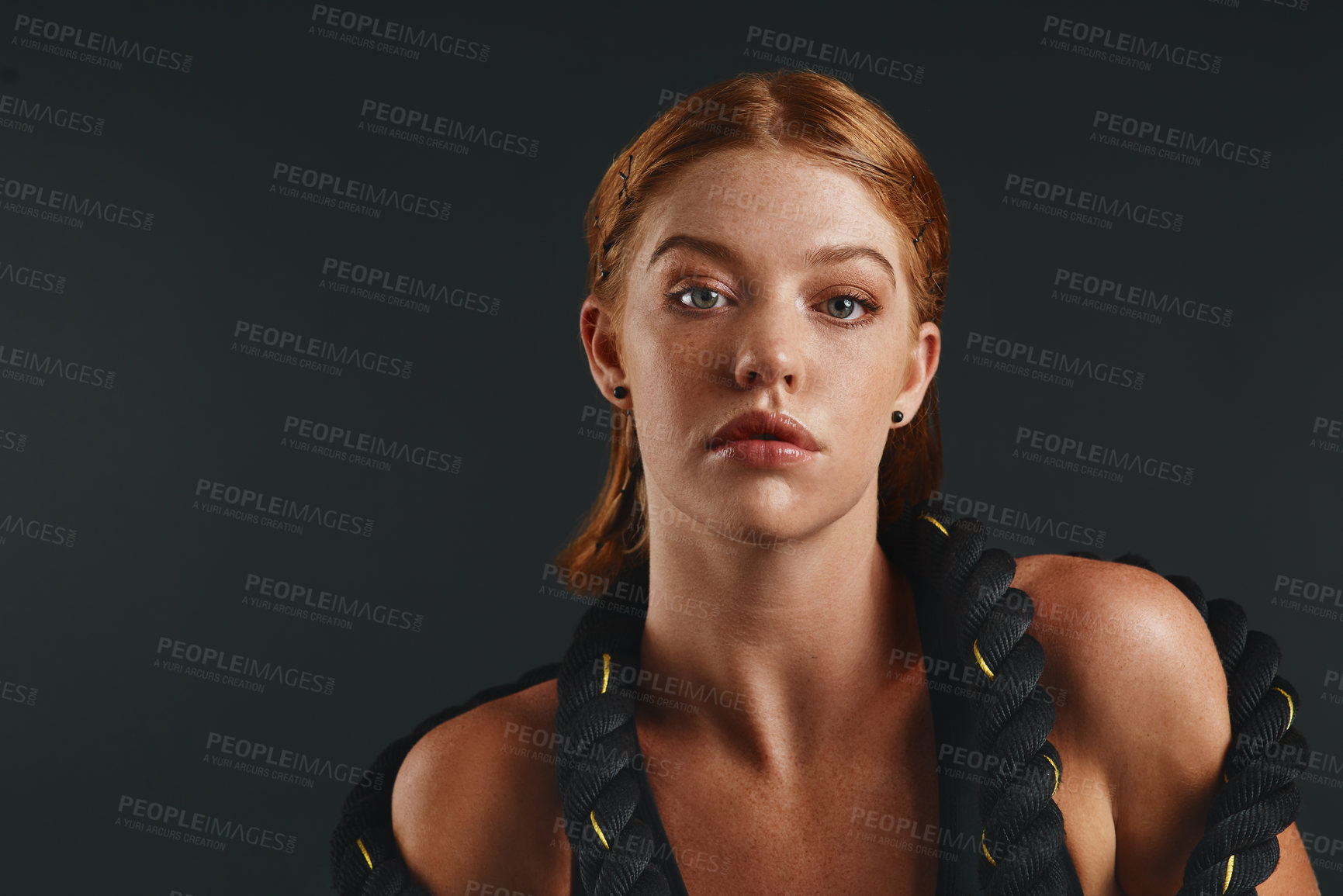 Buy stock photo Studio portrait of a sporty young woman posing with a battle rope against a black background