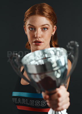 Buy stock photo Studio portrait of a sporty young woman holding a trophy against a black background