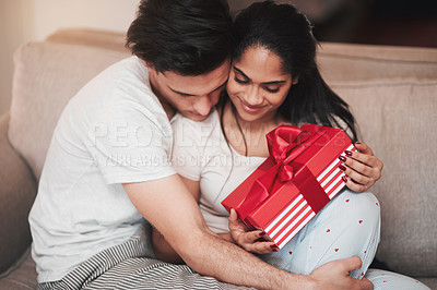 Buy stock photo Cropped shot of a handsome young man hugging his girlfriend on the living room sofa on her birthday