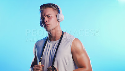 Buy stock photo Studio portrait of a young man posing with a skipping rope and headphones against a blue background