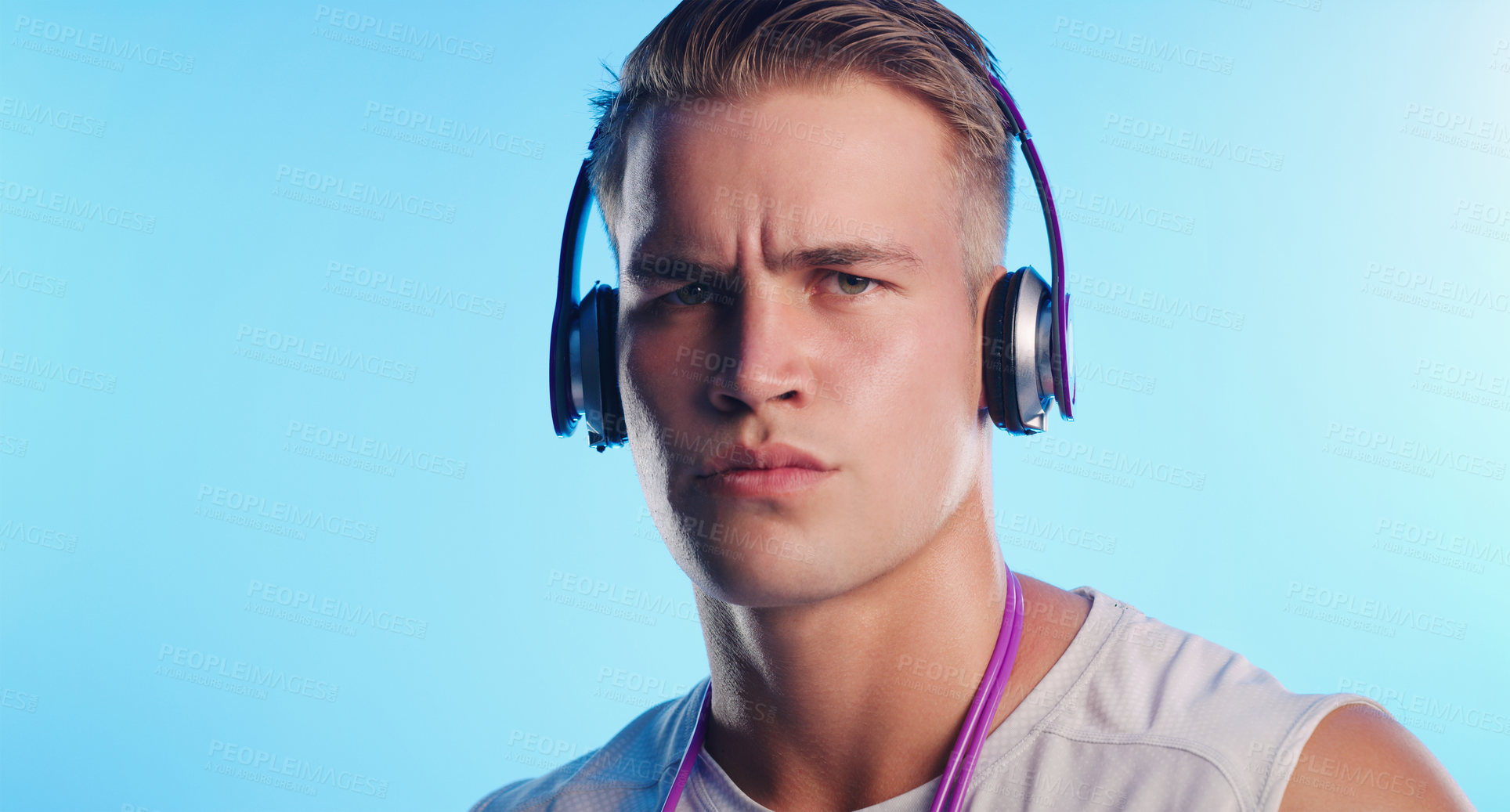Buy stock photo Studio portrait of a young man posing with a skipping rope and headphones against a blue background