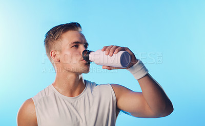 Buy stock photo Studio shot of a handsome young man drinking from a water bottle against a blue background