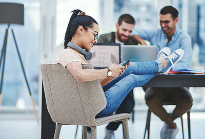 Buy stock photo Shot of a young designer using a cellphone in an office with her colleagues in the background