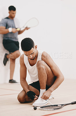 Buy stock photo Shot of a young man tying his shoelaces before a game of squash