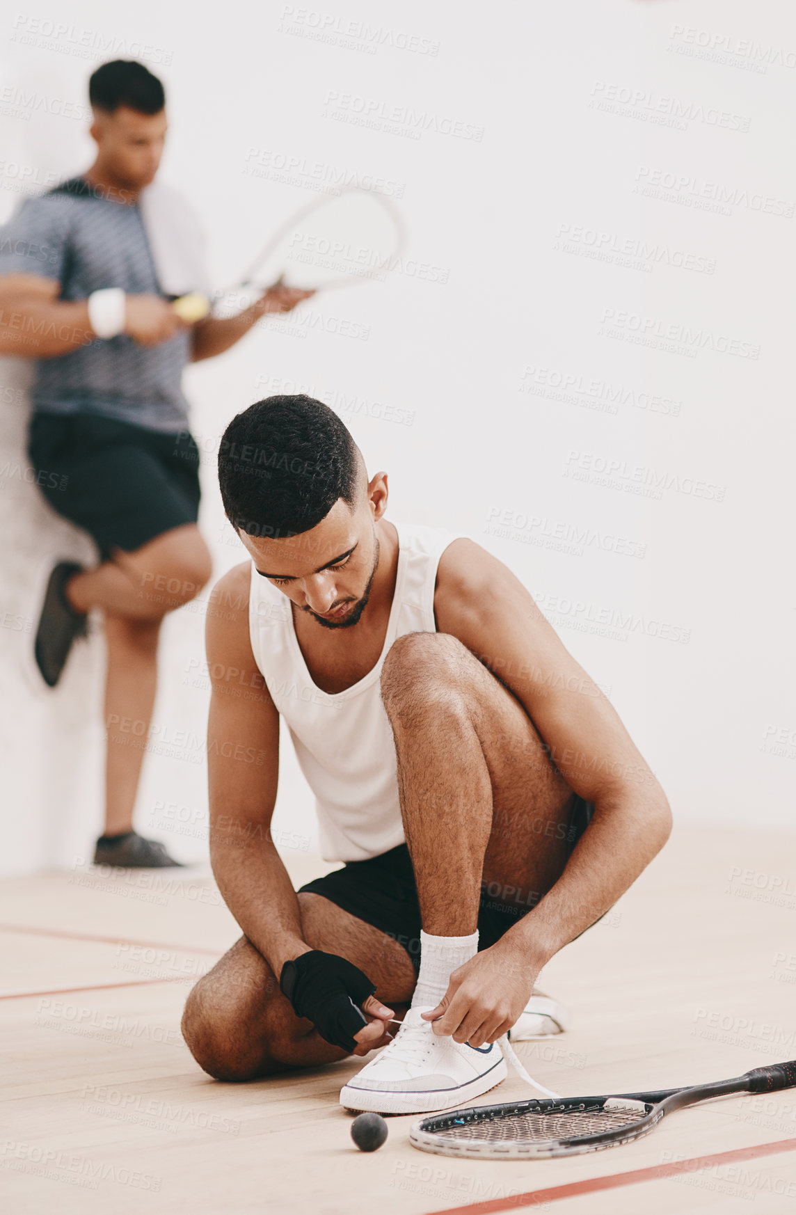 Buy stock photo Shot of a young man tying his shoelaces before a game of squash