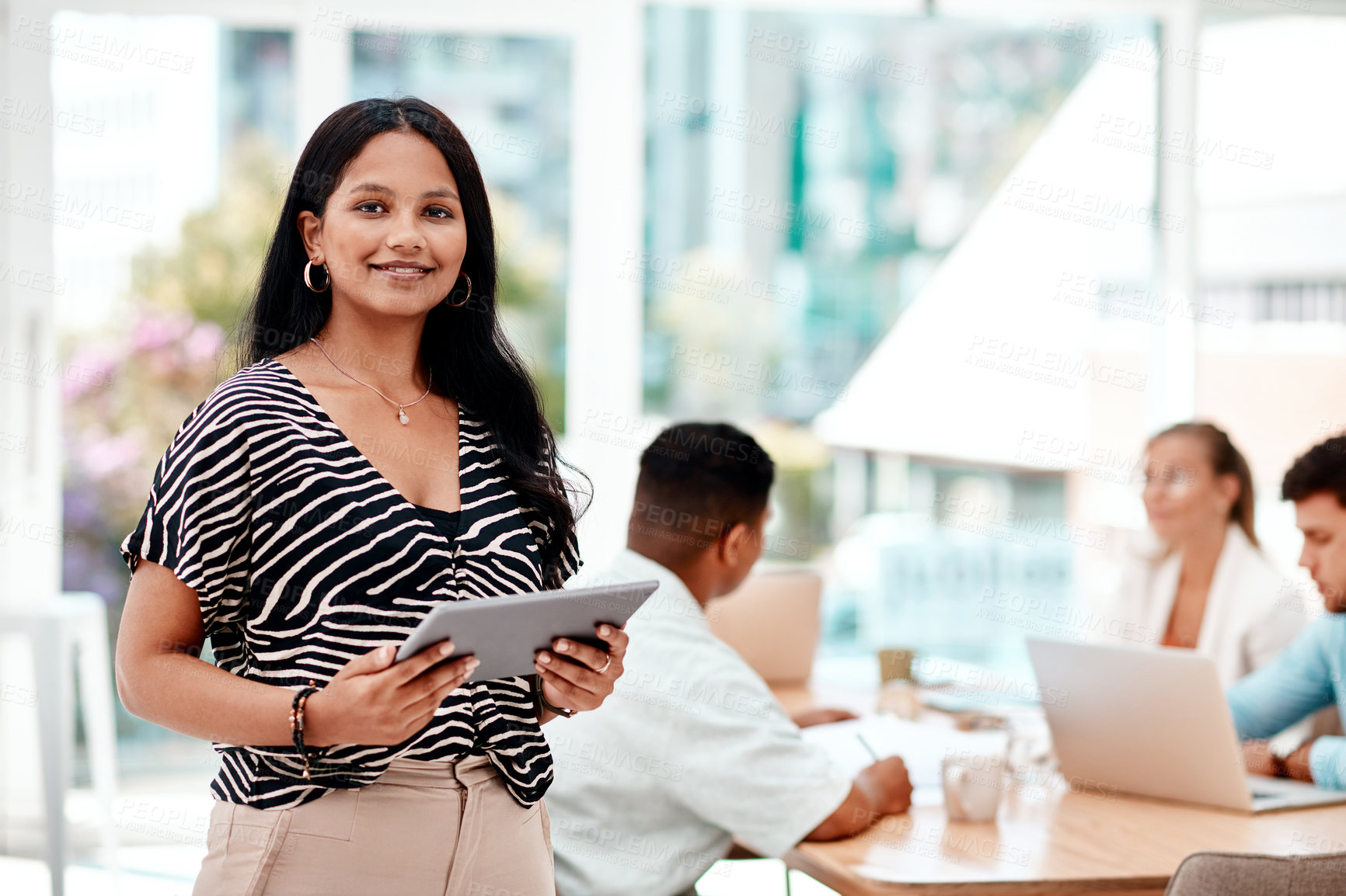 Buy stock photo Cropped portrait of an attractive young businesswoman using her tablet while standing in the boardroom during a meeting