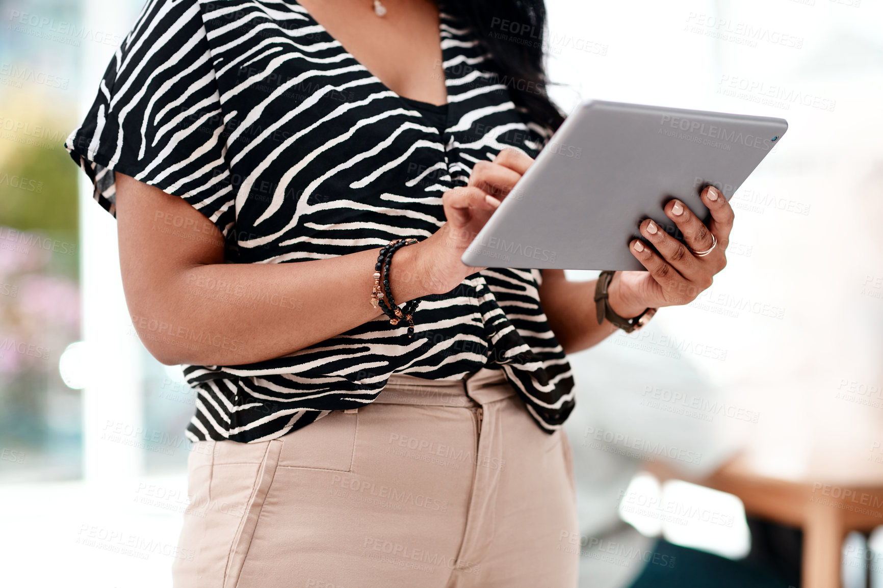 Buy stock photo Cropped shot of an unrecognizable young businesswoman using a tablet while standing in her office