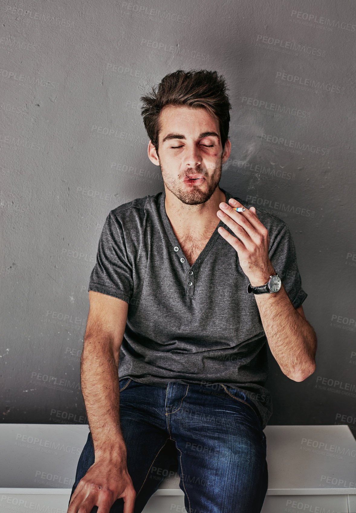 Buy stock photo Cropped shot of a beaten and bruised young man smoking a cigarette
