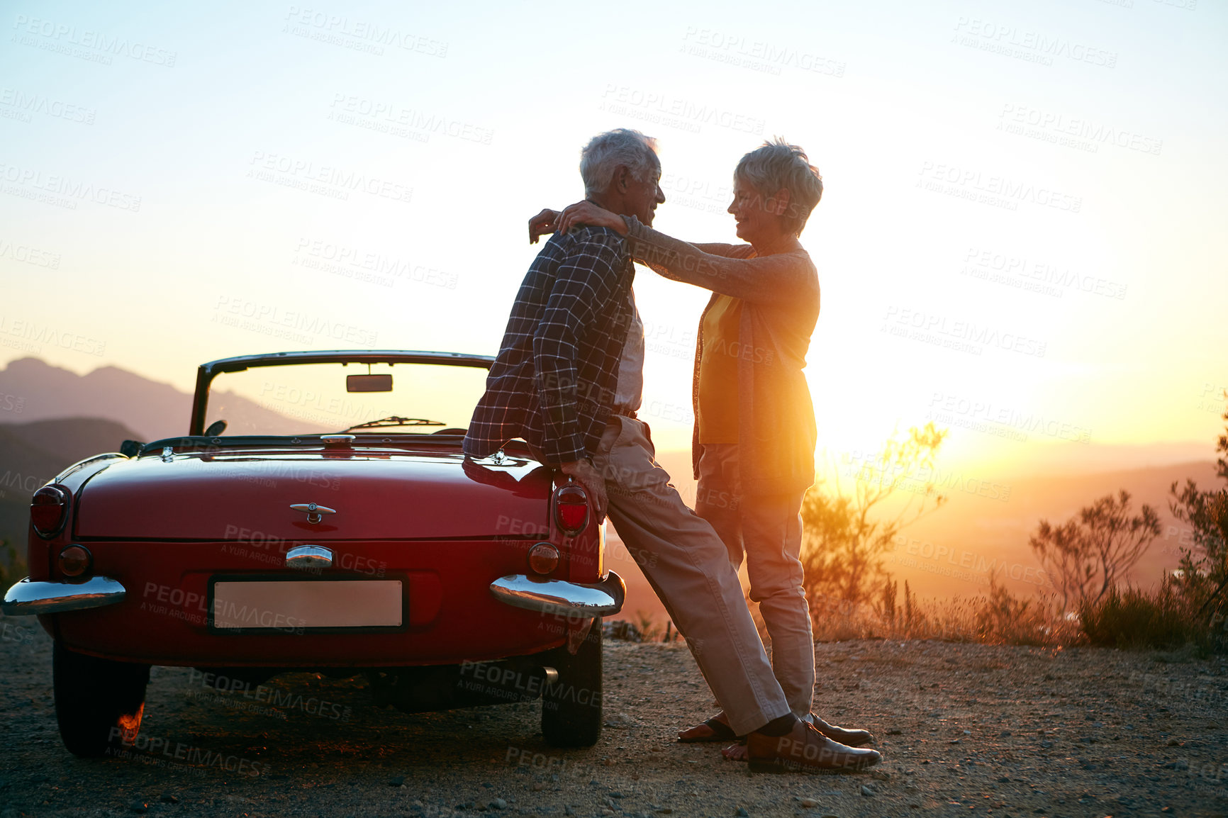 Buy stock photo Shot of an affectionate senior couple enjoying the sunset during a roadtrip