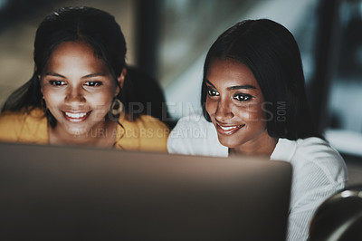 Buy stock photo Shot of two young businesswomen working together on a computer in an office at night