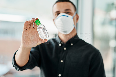 Buy stock photo Shot of a young businessman wearing a mask and using hand sanitiser