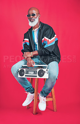 Buy stock photo Studio shot of a mature man holding a boombox while sitting against a red background