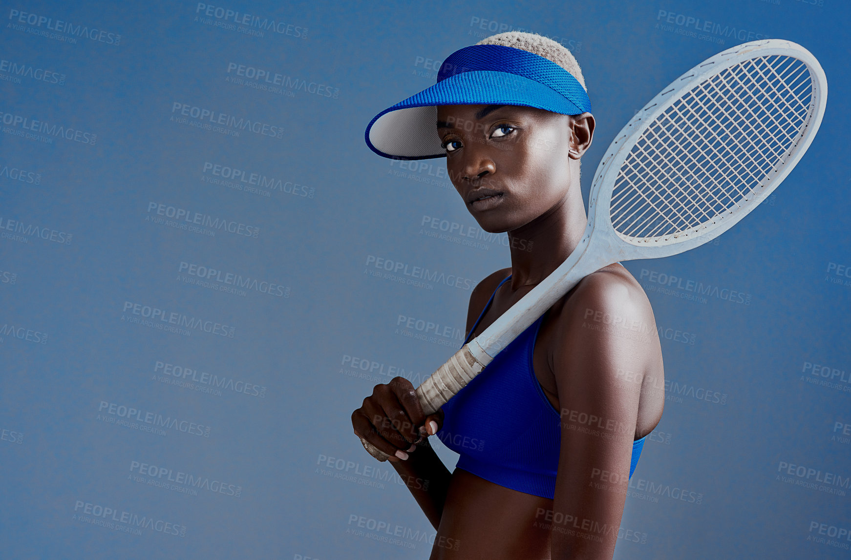 Buy stock photo Serious, black woman and portrait with racket for tennis or professional sport on a blue studio background. Young African, female person or athlete with bat for game, match or competition on space