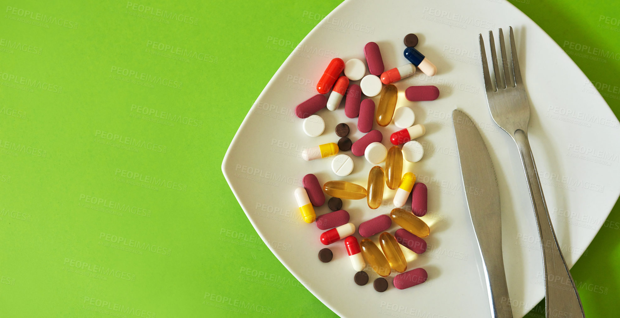 Buy stock photo Studio shot of medication served on a plate with a fork and knife against a green background