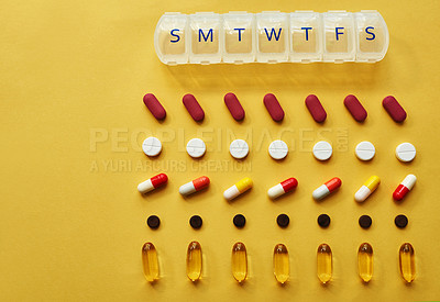 Buy stock photo Studio shot of tablets and a medicine organizer against a yellow background