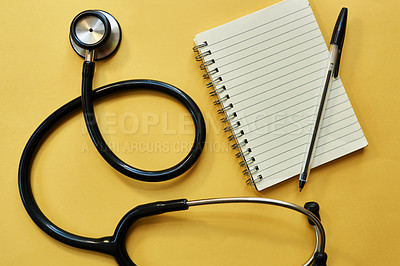 Buy stock photo Studio shot of a stethoscope, notepad and pen gainst a yellow background