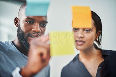 Buy stock photo Cropped shot of two young business colleagues brainstorming on a glass wipe board in their office
