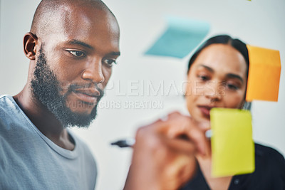 Buy stock photo Cropped shot of two young business colleagues brainstorming on a glass wipe board in their office