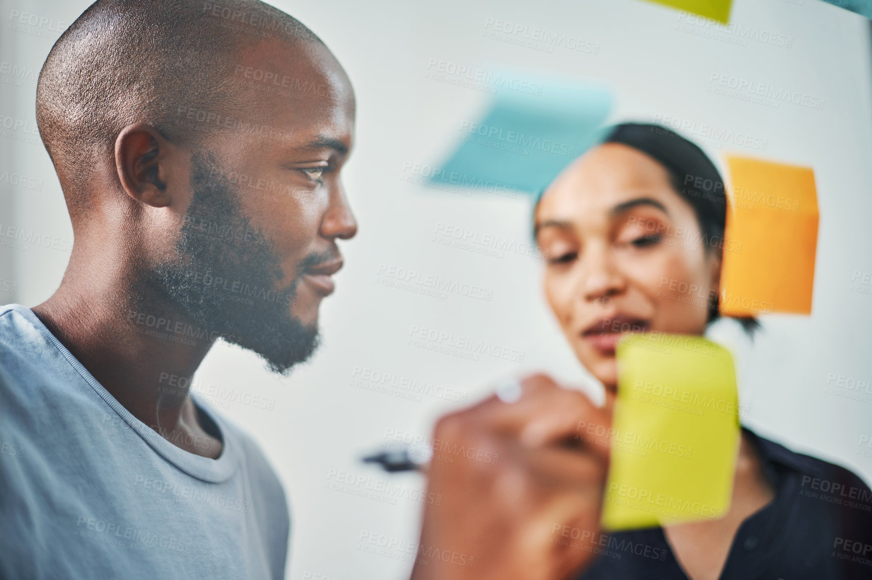 Buy stock photo Cropped shot of two young business colleagues brainstorming on a glass wipe board in their office