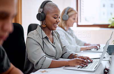 Buy stock photo Shot of a young businesswoman wearing headphones while working on a laptop alongside her colleagues in an office