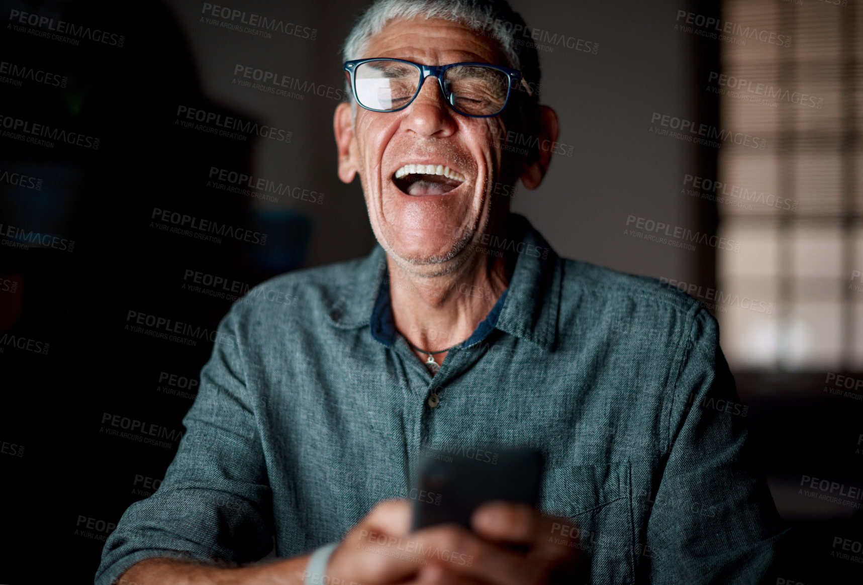 Buy stock photo Shot of a senior businessman using a cellphone in an office at night