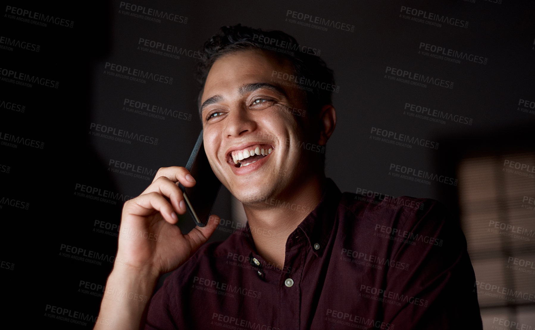 Buy stock photo Shot of a young businessman talking on a cellphone in an office at night