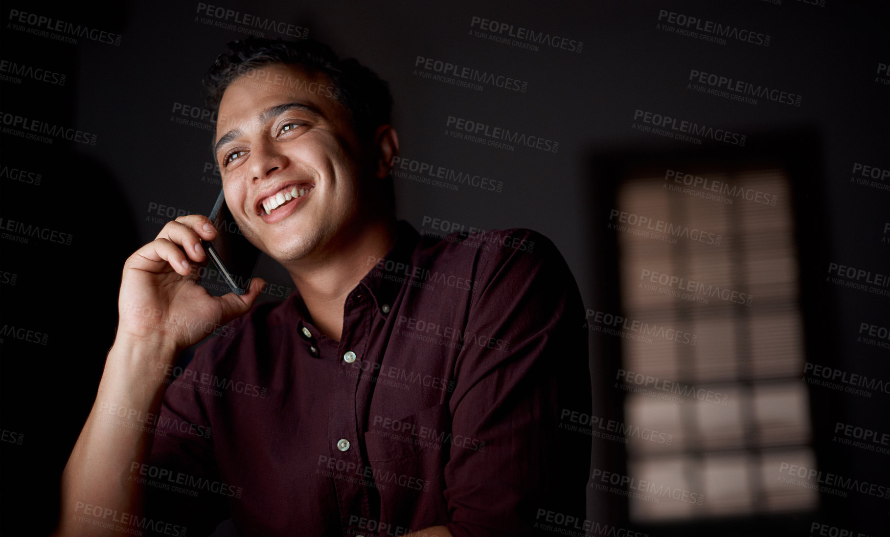 Buy stock photo Shot of a young businessman talking on a cellphone in an office at night