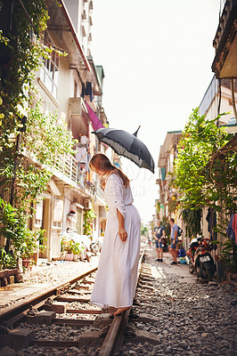 Buy stock photo Shot of a young woman walking on train tracks through the streets of Vietnam