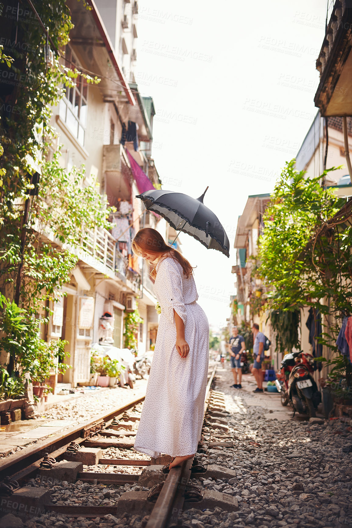 Buy stock photo Shot of a young woman walking on train tracks through the streets of Vietnam