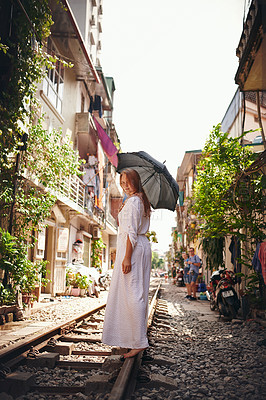 Buy stock photo Shot of a young woman walking on train tracks through the streets of Vietnam