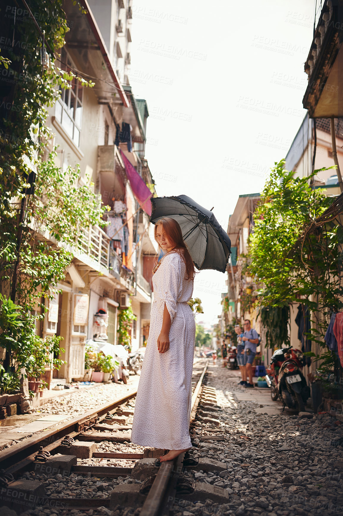 Buy stock photo Shot of a young woman walking on train tracks through the streets of Vietnam