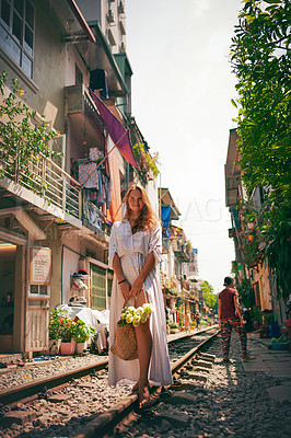 Buy stock photo Shot of a young woman walking on train tracks through the streets of Vietnam