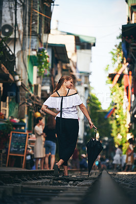 Buy stock photo Shot of a young woman holding an umbrella while exploring a foreign city on a sunny day