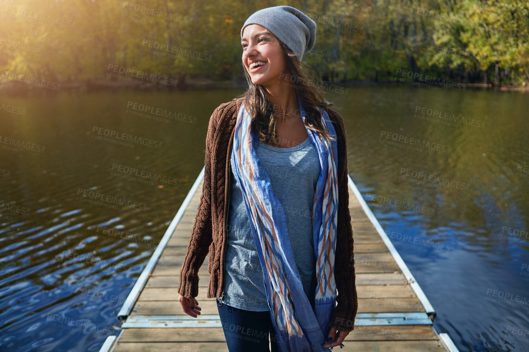 Buy stock photo Shot of a happy young woman standing on a pier next to a lake