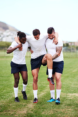 Buy stock photo Shot of young men carrying their team mate off the field after injuring his knee during a rugby game