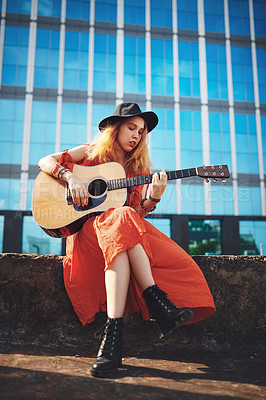 Buy stock photo Shot of a beautiful young woman playing the guitar while out in the city